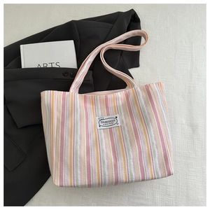 Close-up of pastel striped canvas tote bag with fashion label and art book accessory