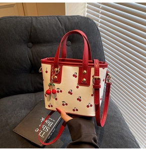 Detail of white cherry print tote bag featuring a cute cherry charm and red handles