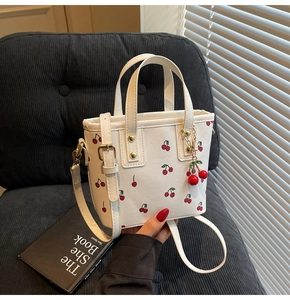 Detail of white cherry print bucket bag with gold hardware and cherry charm pendant