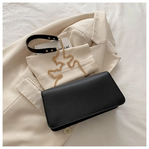 Vue détaillée du sac à bandoulière noir avec chaîne dorée posé sur un blazer beige