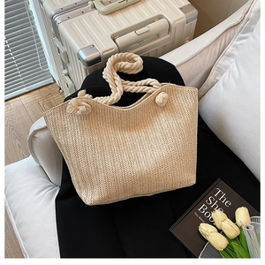Close-up of beige woven straw shoulder bag with textured herringbone pattern and cotton rope handle