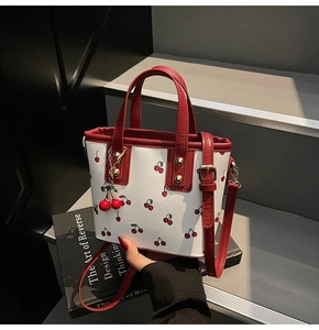 Detail of white cherry print tote bag featuring red leather handles and cherry charm