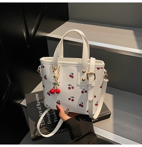 Detail of white mini tote bag with cherry prints and a 3D cherry charm on books
