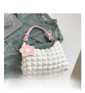 Detail of white bubble pleated crossbody bag with pink woven handle and flower charm