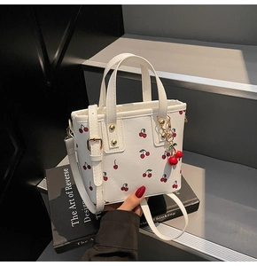 Detail of white cherry print tote bag featuring gold hardware and a 3D cherry charm
