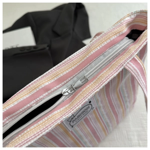 Detail of striped canvas tote with top metal zipper and fashion patch decoration
