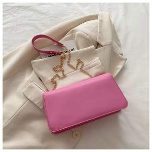 Détail du sac bandoulière rose vif en cuir avec chaîne dorée sur un blazer beige