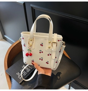 Detail of white cherry print bucket bag with gold hardware and cherry charm on black chair