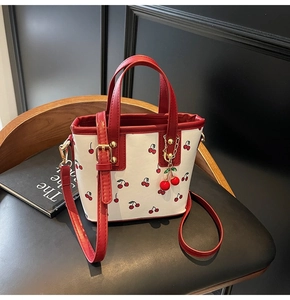 Detail view of mini cherry print tote bag with red handles and metal cherry charm decoration