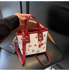 Close-up of stylish cherry print tote bag with red leather trim and a cherry pendant