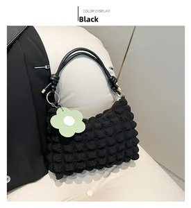 Close-up of black bubble textured dumpling bag with a green flower charm on a sofa