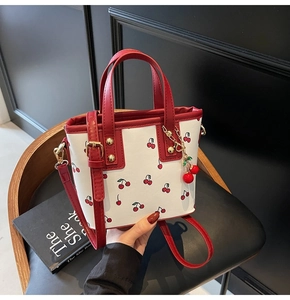 Dettaglio della borsa tote bianca con stampa ciliegie, manici rossi e rivetti dorati