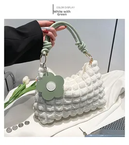 Detail of white pleated handbag with light green knotted handle and floral charm