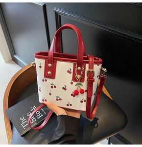 Close-up of white cherry print tote bag with red handles and cute cherry charm accessory
