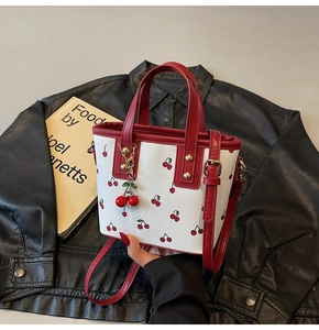 Detail of white cherry tote bag with red leather trim and charm on black leather jacket