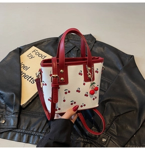 Macro detail of bucket bag with cherry print and red leather handle on a book background