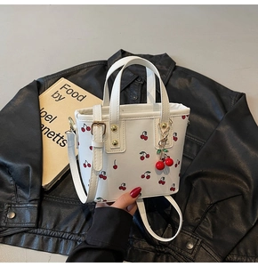 Detail of white cherry print handbag with gold rivets and metallic cherry pendant