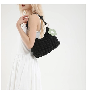 Close-up of black bubble textured underarm bag with a green flower charm on model