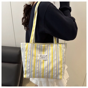 Detail view of striped canvas tote bag with FASHION patch on a model in a room