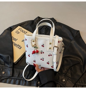 Detail of white leather cherry print handbag with gold rivets and cherry pendant