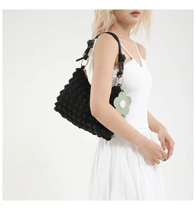 Detail of black bubble textured crossbody bag with knotted strap and green floral charm