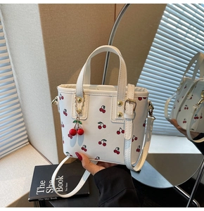 Detail view of white cherry print tote bag with golden hardware and cherry pendant charm
