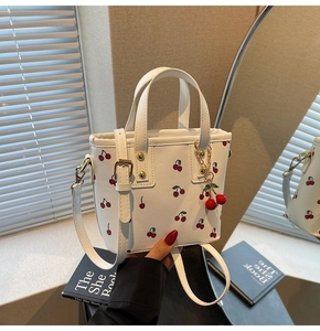 Detailed view of white cherry print tote bag with removable strap and cherry charm accessory