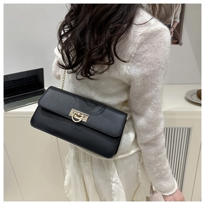Détail d'un sac à rabat noir avec chaîne dorée porté sur un pull blanc élégant