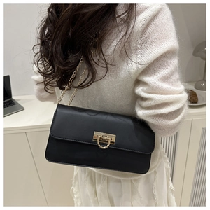 Sac baguette en cuir noir mat avec bandoulière chaîne dorée porté par un mannequin chic