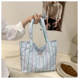 Detail of blue and purple striped canvas tote bag with a fashion logo patch on the front