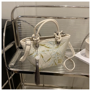 Detail view of embroidered bucket bag with green leaf texture and stylish tassel pendant
