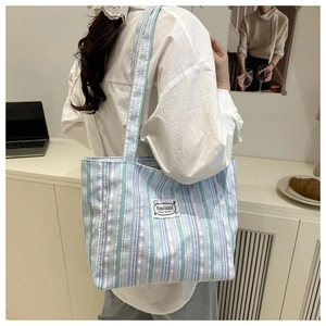 Detail view of large striped canvas tote bag with fashion patch on shoulder of model