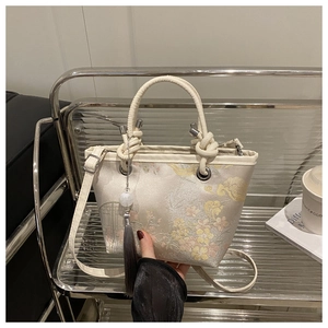Detail of floral jacquard embroidery on cream bucket bag with gray tassel accent