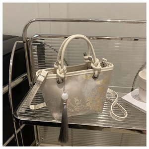 Detail of embroidered floral patterns and tassel on an elegant cream bucket bag