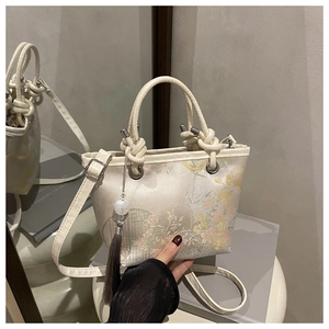 Detail of cream jacquard bucket bag with floral embroidery and elegant tassel accent