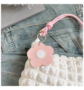 Detail of white pleated shoulder bag with pink floral pendant on denim background