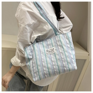 Vertical striped canvas tote bag with fashion label shown carried on model's shoulder