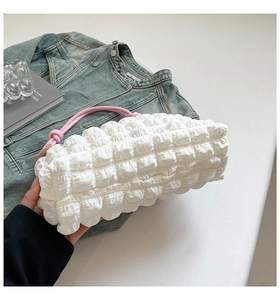 Detail of white bubble quilted handbag with pink tubular handles on a white table