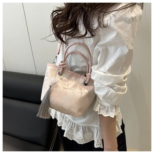 Detail of embroidered bucket bag with round handle and tassel held by a model