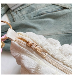 Detail of white pleated texture fabric with gold zipper and metal ring on shoulder bag