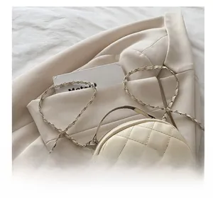 Detail of cream quilted mini backpack with woven chain strap on a beige blazer