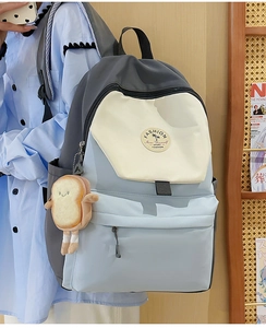 Detail of color-block backpack with blue and beige panels and a cute plush toast charm