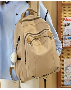 Detailed side view of a large beige nylon student backpack with a cute plush doll charm