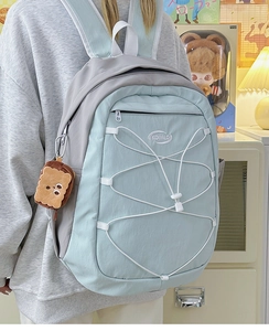 Gros plan d'un sac à dos en toile bleu et gris avec cordon blanc et pendentif toast