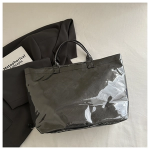 Gros plan d'un cabas noir brillant sur tissu beige avec accessoires modernes