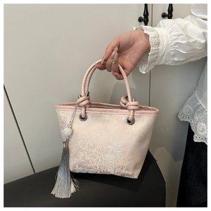 Detail of pink embroidered silk bucket bag with long grey tassel and woven handle
