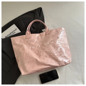 Détail du sac cabas rose brillant avec texte blanc posé sur un tissu de fond blanc cassé