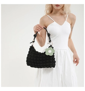 Close-up of black bubble textured dumpling bag with leather handle and green flower charm