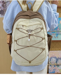 Détail d'un sac à dos crème et marron avec des sangles élastiques croisées sur le devant