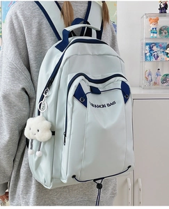Detailed view of grey-blue canvas backpack with navy trim and cute cloud plush pendant
